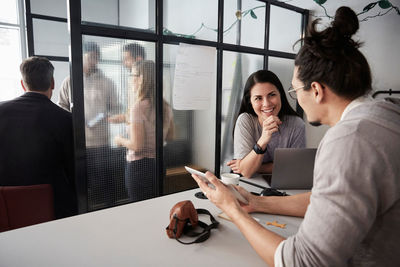 Male entrepreneur discussing with smiling female colleague over digital tablet at desk in office