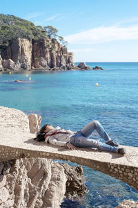 Rear view of a woman relaxing in front of blue sea, lying on bridge