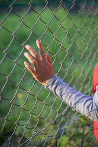 Cropped image of man by chainlink fence against blurred background