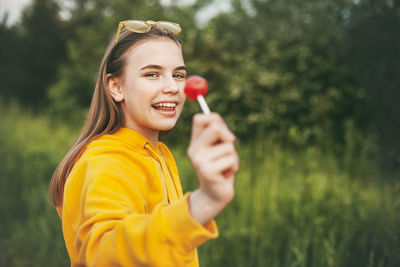 Portrait of smiling girl holding lollipop while standing against plants in park