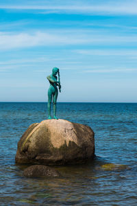 Man standing on rock by sea against sky