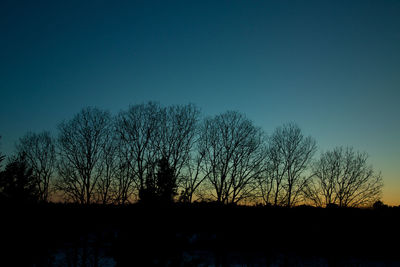 Silhouette trees on field against clear sky during sunset