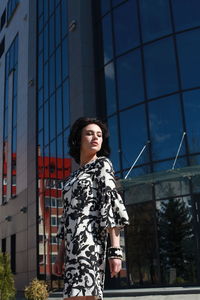 Fashionable young woman wearing floral patterned dress standing against building in city