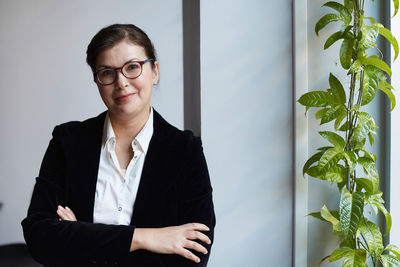 Portrait of smiling mature businesswoman leaning on wall in office