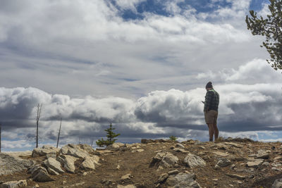 Male hiker standing on mountain with cell phone and dramatic clouds