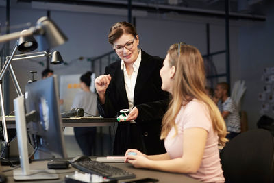 Creative businesswoman looking at female bank manager holding solar toy car in creative office