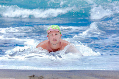 Portrait of shirtless man in cap swimming in sea