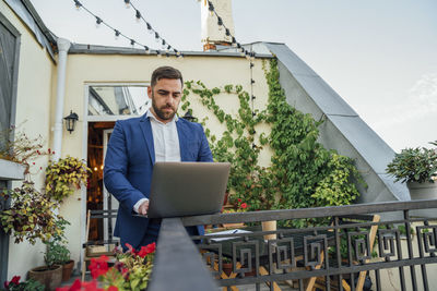 Businessman using laptop on railing at office balcony