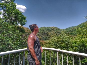 Side view of man standing by railing against sky