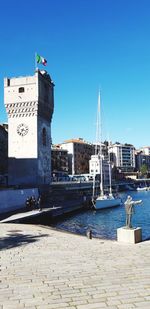 Sailboats in harbor by buildings against clear blue sky