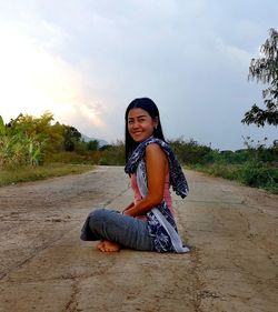 Portrait of smiling young woman sitting against sky