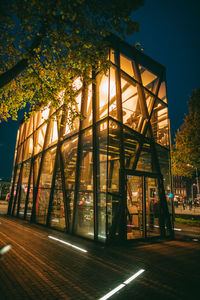 Illuminated street by building against sky at night