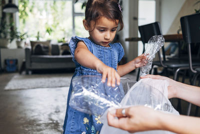 Girl helping daughter collecting crushed plastic bottle in garbage bag at home