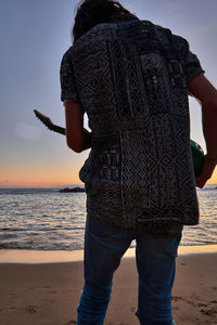 Rear view of woman standing at beach during sunset