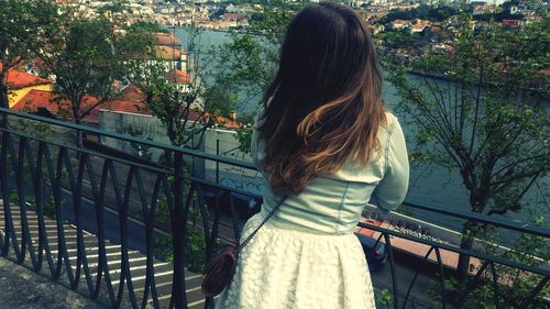 Rear view of woman standing by railing against river in town