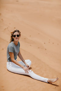 Woman wearing sunglasses sitting on sand at beach