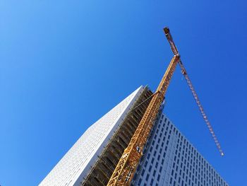 Low angle view of crane by building against clear blue sky