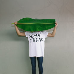 Woman covering face with banana leaf standing against gray background