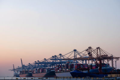 Cranes at commercial dock against clear sky during sunset