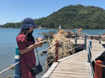 Woman using mobile phone by sea against sky