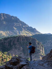 Full length of man on rock in mountains against clear sky