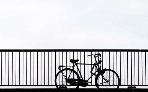 Silhouette of bicycle on bridge against clear sky