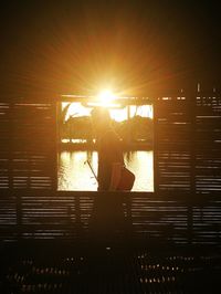 Silhouette man sitting by sea against orange sky