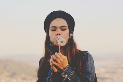 Portrait of woman holding hat against sky