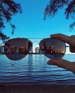 Cityscape by river seen through sunglasses held by person