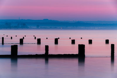 Wooden posts in sea against sky at sunset