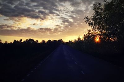 Road amidst silhouette trees against sky at sunset