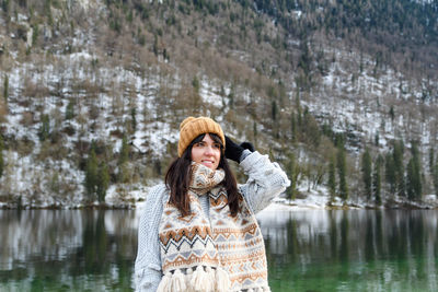 Young woman in winter sweater smiling, standing by a lake.