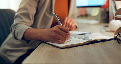 Midsection of woman writing in book at table