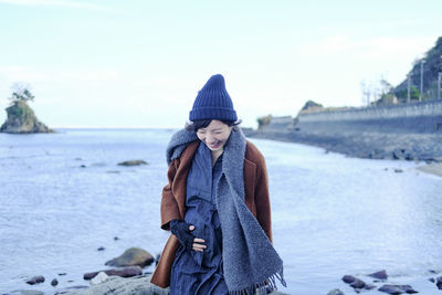 Cheerful woman wearing warm clothes while standing on rock against sky