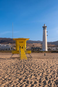 Lighthouse by sea against clear blue sky