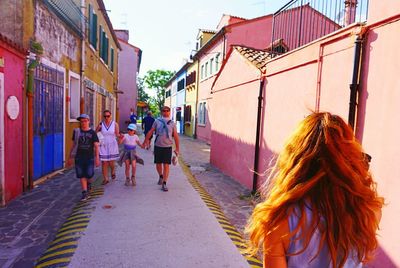 Rear view of people walking on road along buildings