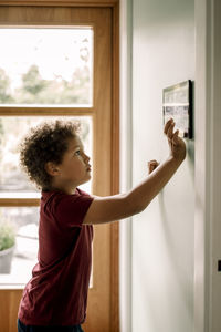 Side view of boy using home automation through tablet pc mounted on wall
