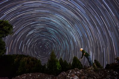 Long exposure of man standing on rock against star trail