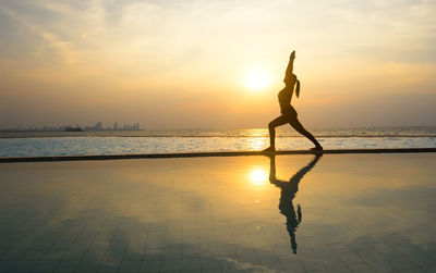 Man surfing in sea against sky during sunset