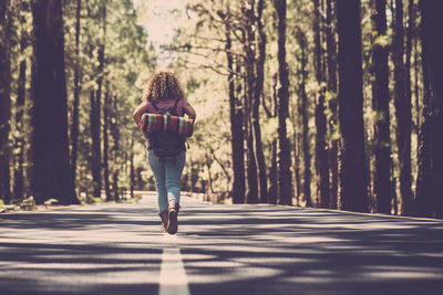 Rear view of woman walking on road amidst trees in forest