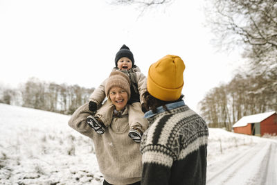 Happy woman with daughter sitting on shoulder looking at girlfriend