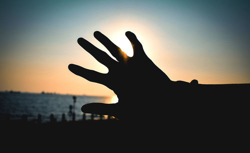 Silhouette hand against sky during sunset