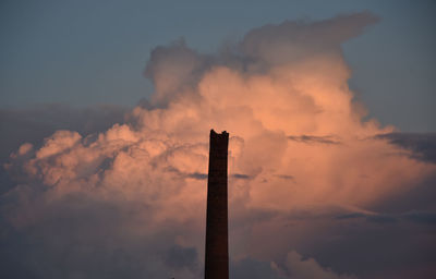 Low angle view of smoke stacks against sky during sunset