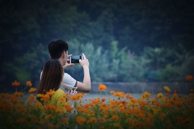 Couple photographing with mobile phones while standing by flowers