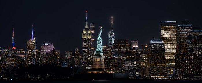 Illuminated buildings and statue of liberty in city at night
