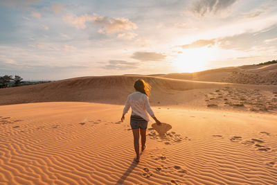 Rear view full length of man walking at desert during sunset