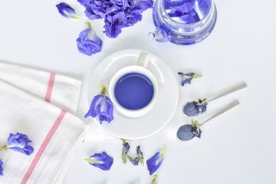 High angle view of purple flowers by herbal tea on white table