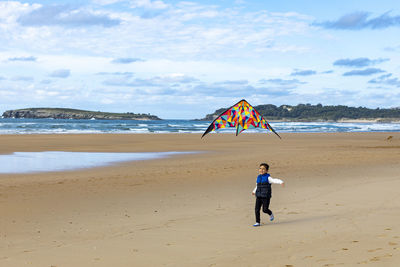 Cute boy playing with kite at shore of beach