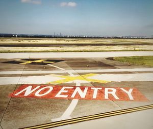 Road sign at airport against sky