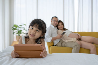 Asian pregnant family with young daughte watching cartoon from computer together in bedroom